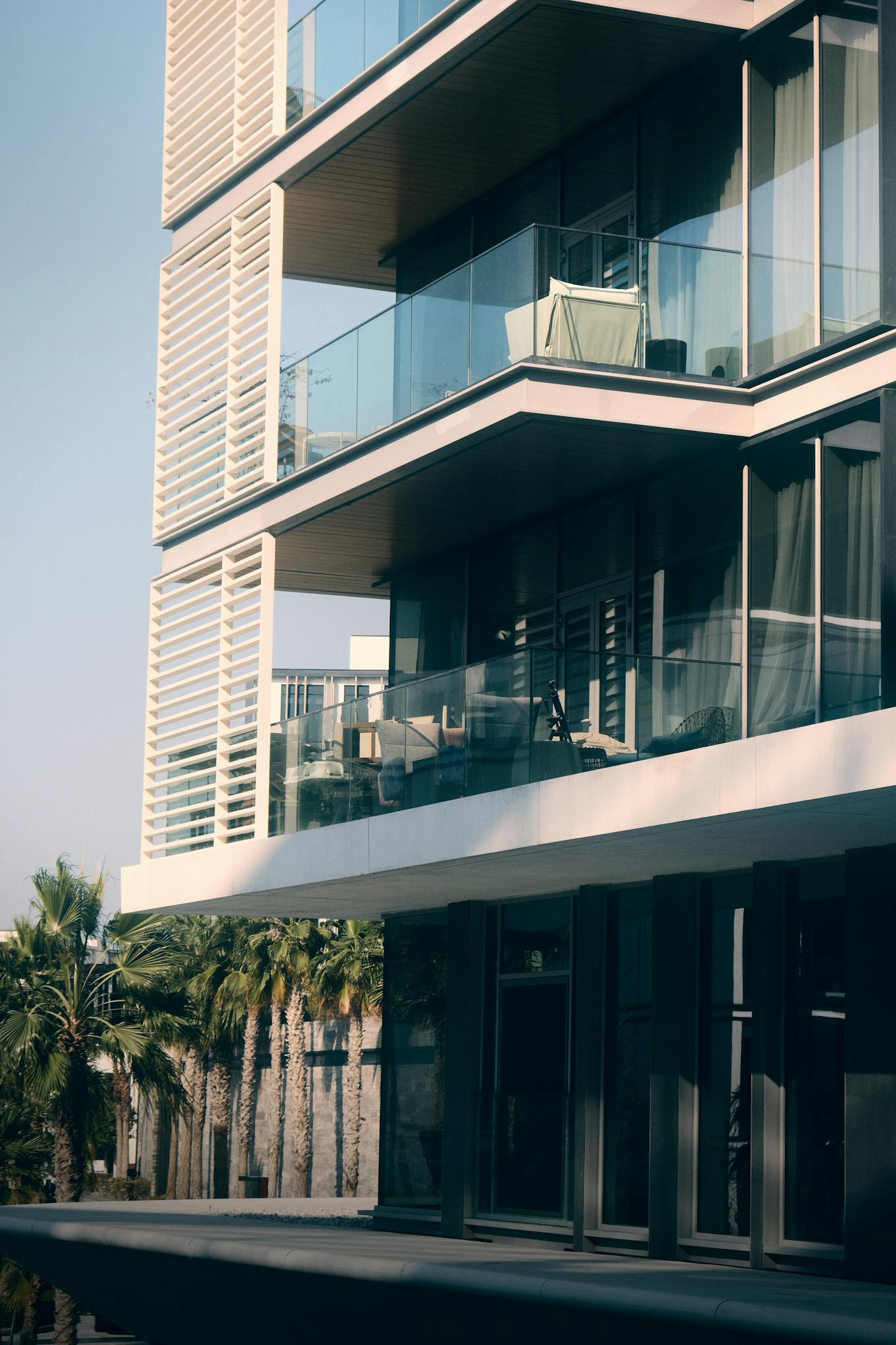 Contemporary apartment building with glass balconies, surrounded by palm trees, highlighting urban elegance.